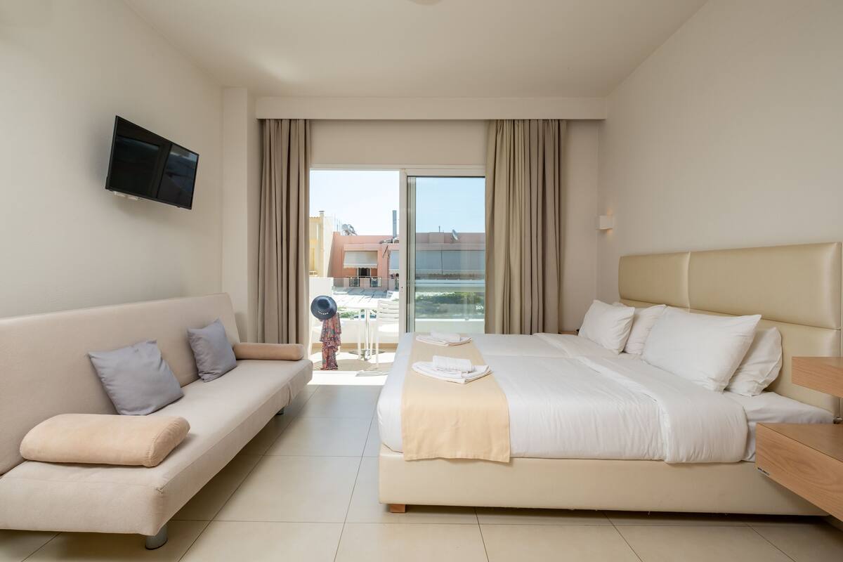 Une chambre d’hôtel avec un lit, un canapé, une télévision et un balcon offrant une vue.