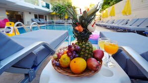 A poolside table with a fruit basket, a pineapple, and two glasses of orange juice. - Dimitrios Beach Hotel Adults Friendly 14 plus (Rethymno)