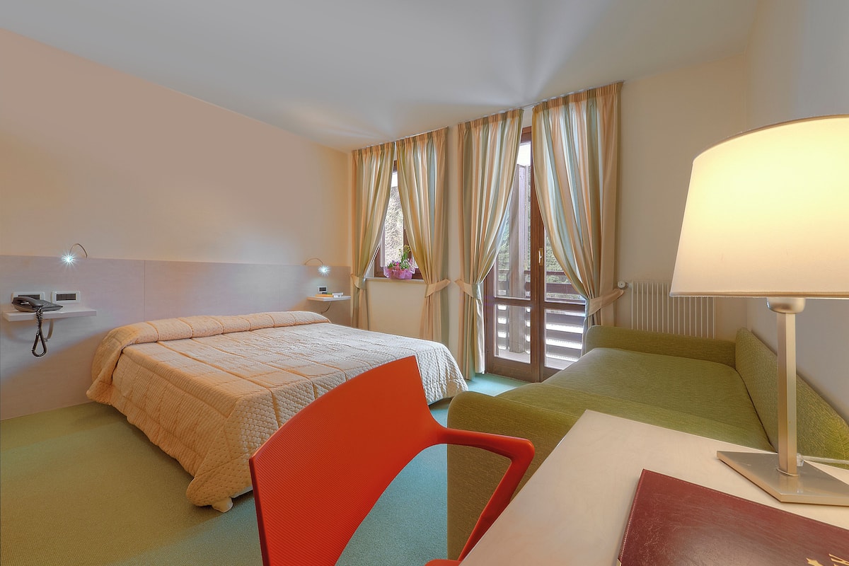 A hotel room with two beds, a desk with a lamp, a chair, a phone on a shelf, and a window with curtains.