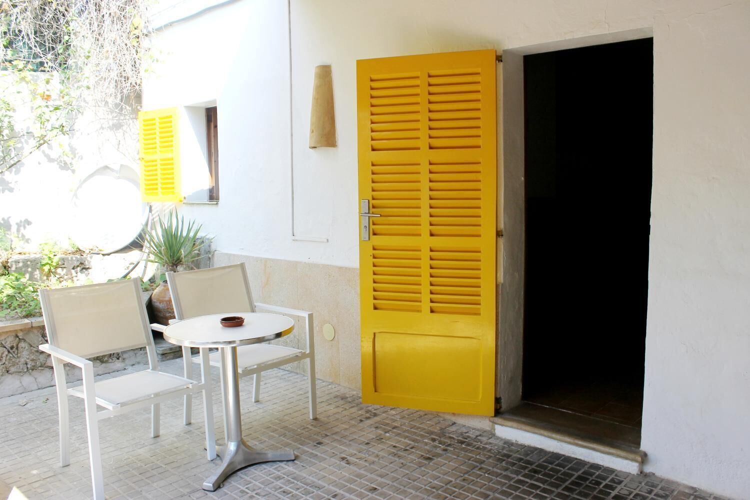 A room with a white wall, a yellow door, a round table with two chairs, and a potted plant.