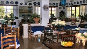 A dining area with wooden chairs and tables, potted plants, and a variety of decorative items. - Hostal Residència Catalina Vera (Andraitx)