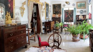 A room with a wooden dresser, a red chair, a spinning wheel, and various decorative items including plates and paintings. - Hostal Residència Catalina Vera (Andraitx)