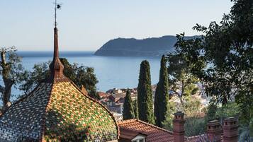 A building with a tiled dome roof, a stone balustrade, and a view of the sea and hills in the background.