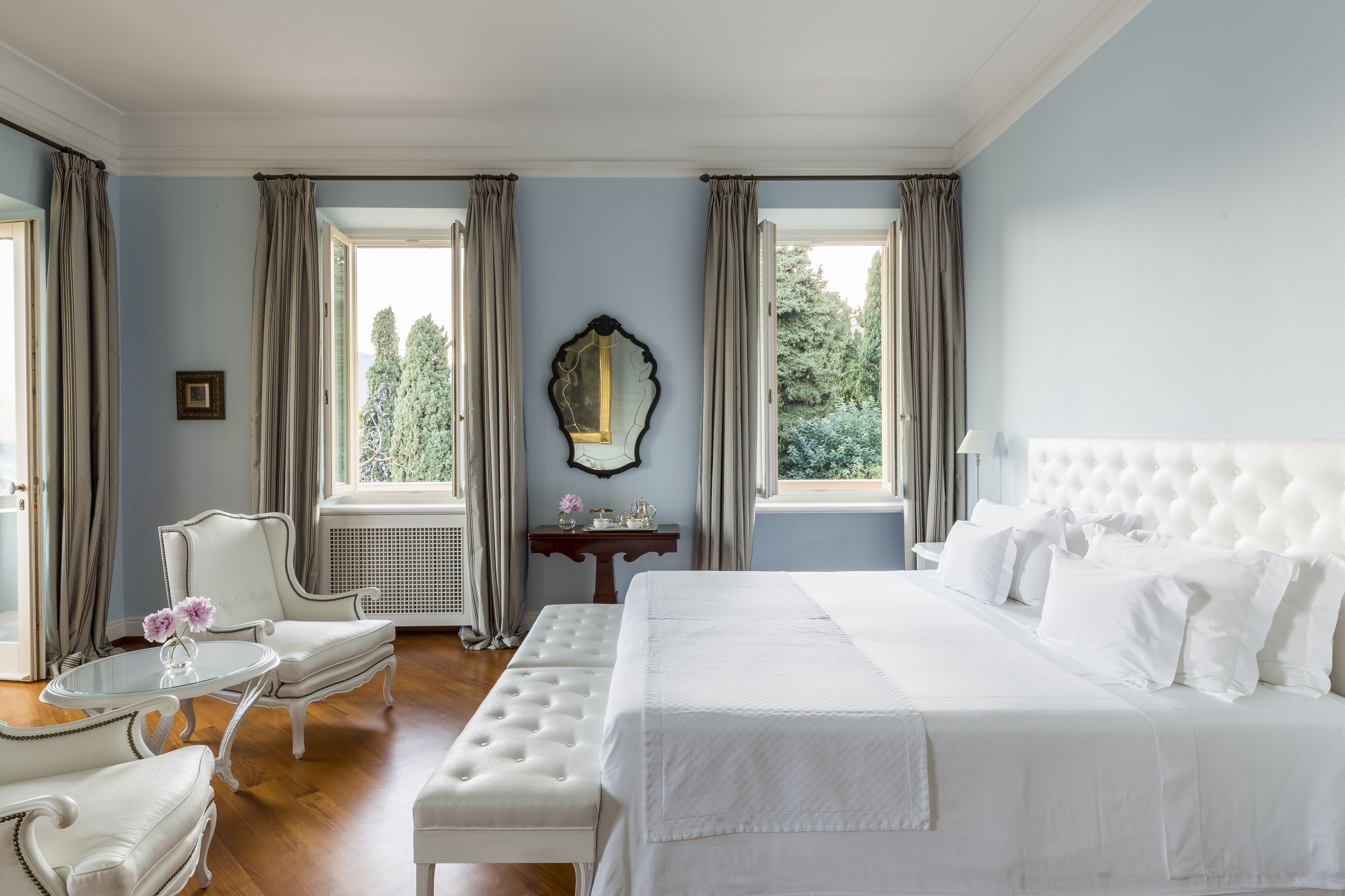A bedroom with a large bed, a chair, a table, and a mirror.