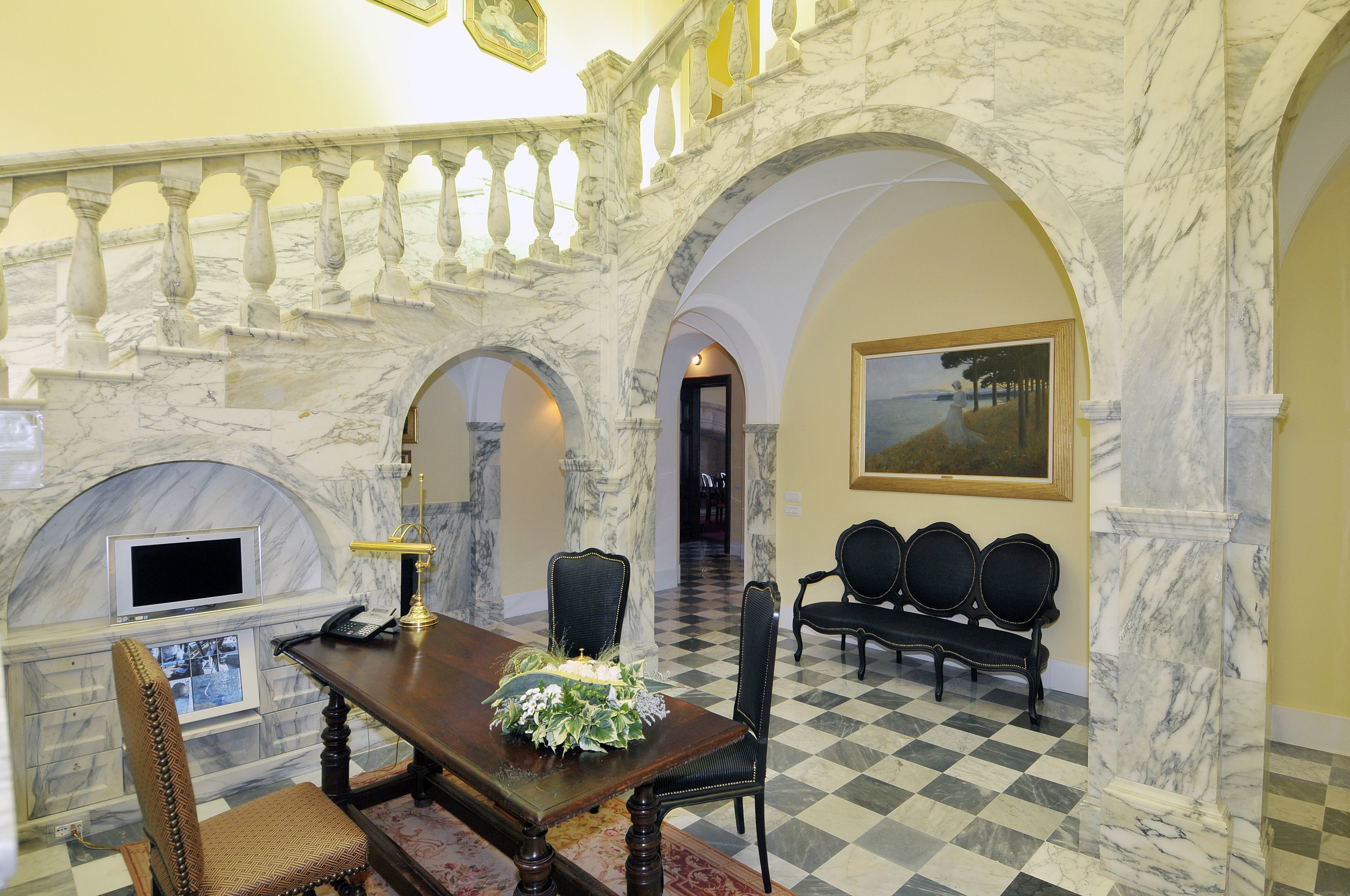 A marble-floored room with a checkered floor, a wooden table with chairs, a fireplace, and a framed painting on the wall.