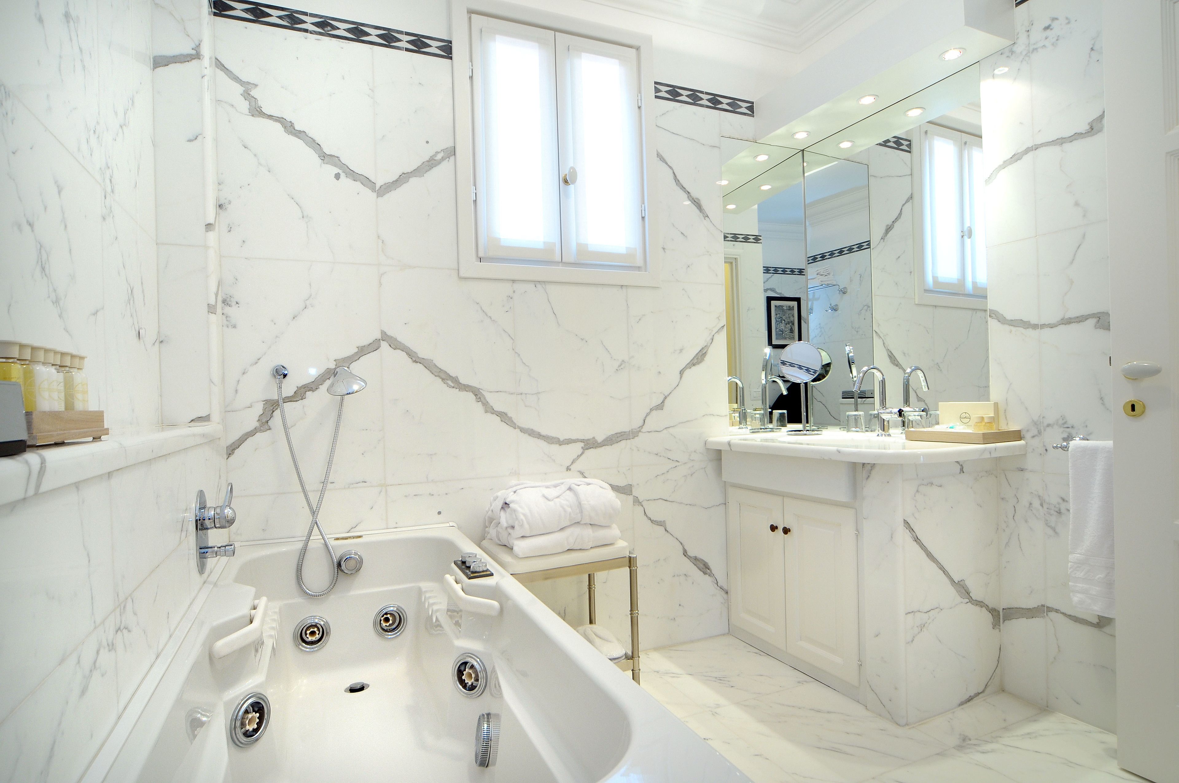 Un baño moderno con suelo de mármol, una bañera independiente, un tocador con espejo y un perchero para toallas.