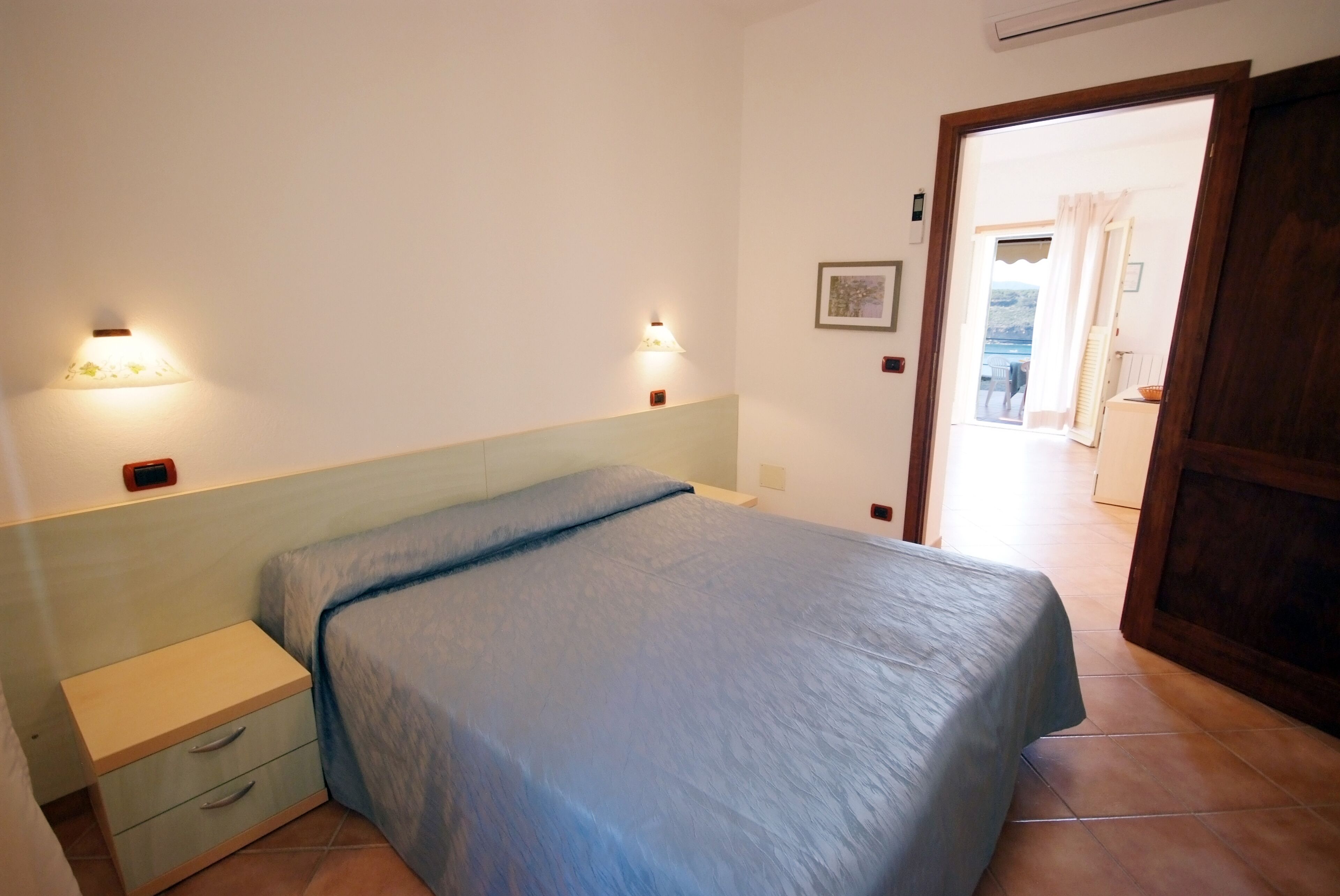 Un dormitorio con cama, mesitas de noche y lámparas de pared.