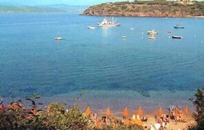 A coastal scene with boats on the water and beach umbrellas in the foreground. - Hotel Dino (Capoliveri)