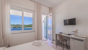 Ein Hotelzimmer mit Bett, Schreibtisch mit Fernseher, Stuhl und Balkon mit Meerblick.
