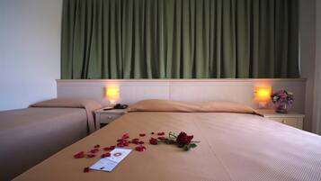 A hotel room with a large bed, two bedside tables, a nightstand, and a green curtain.