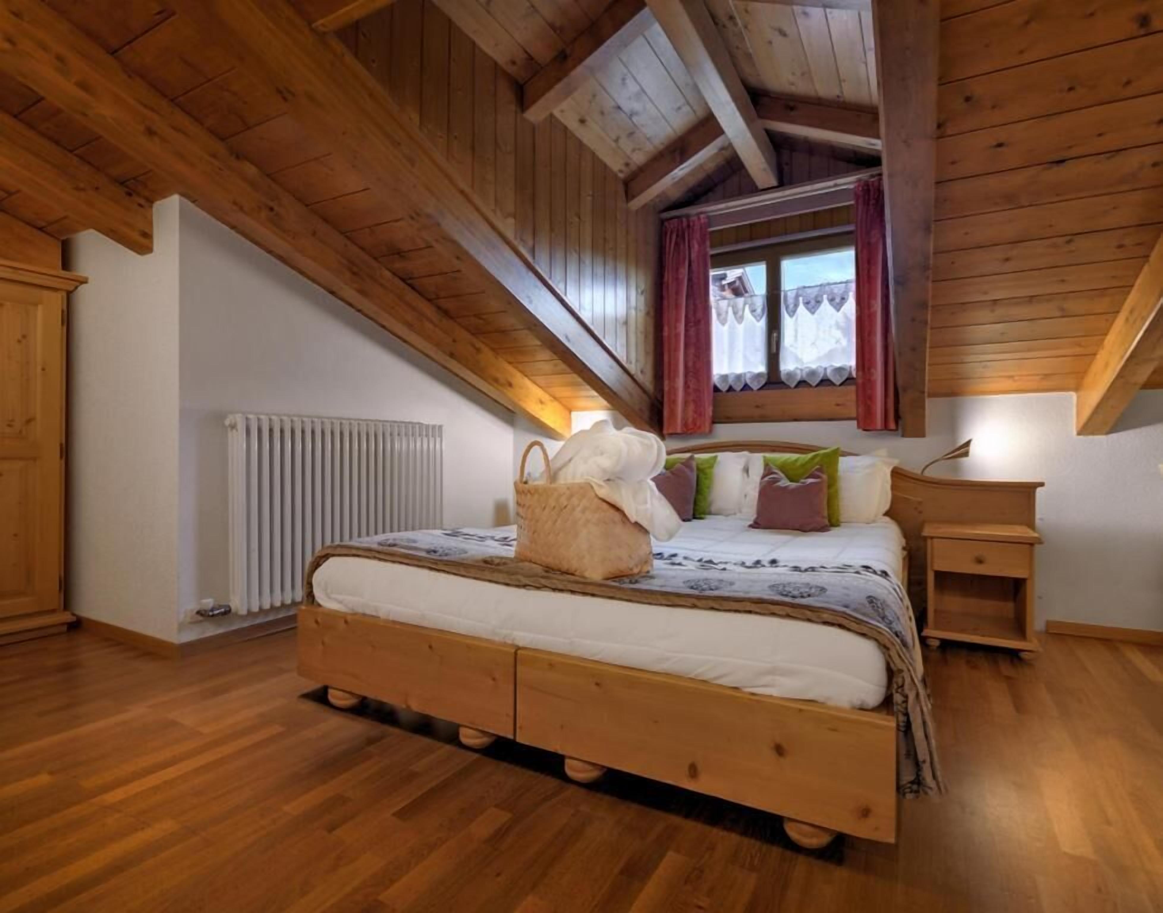 A wooden-framed attic bedroom with a bed, a radiator, and a window with curtains.