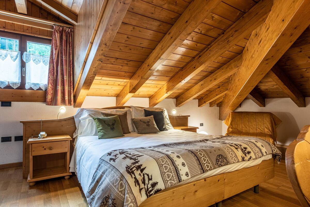 A bedroom with a wooden ceiling, a bed with patterned bedding, and a nightstand with a lamp.