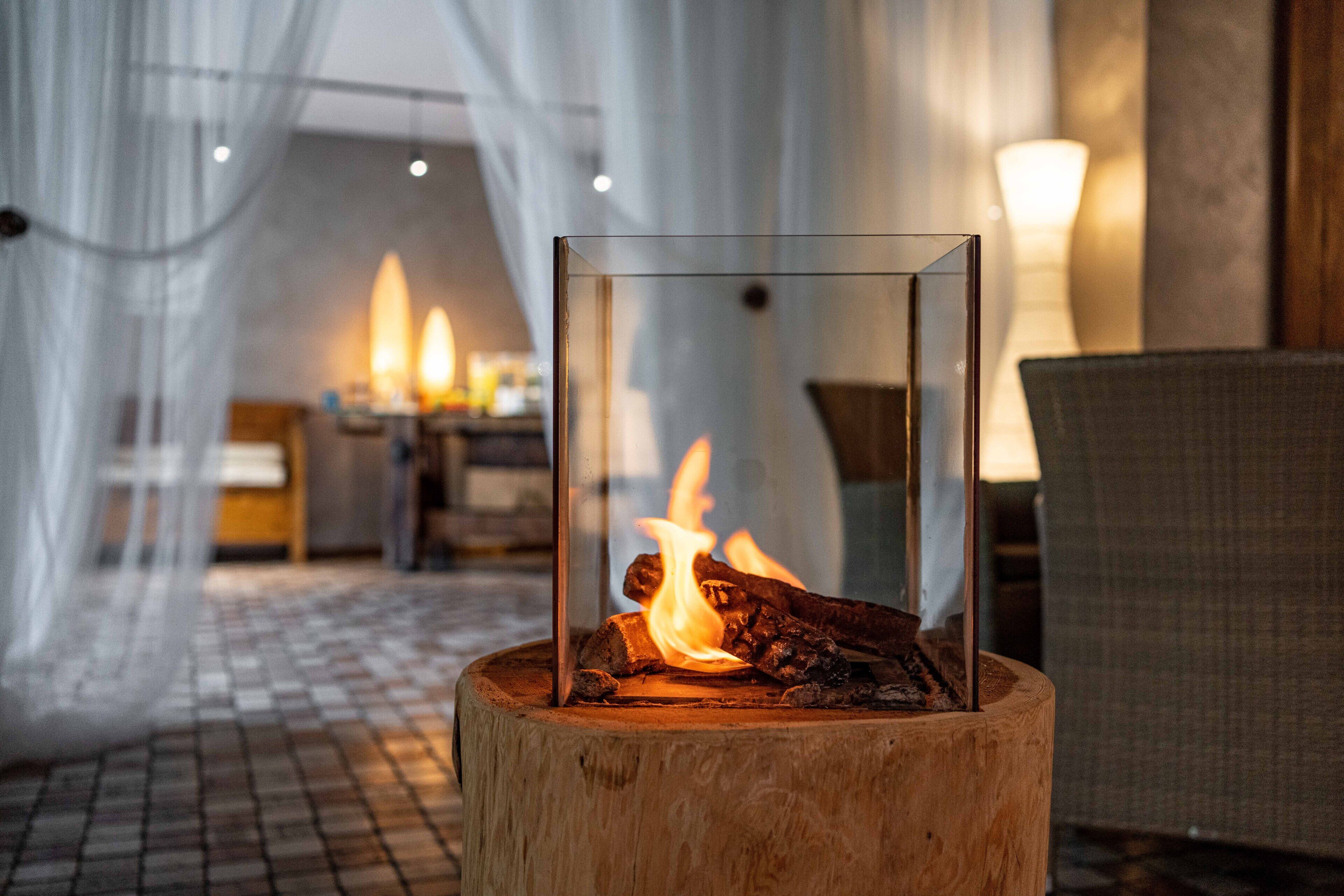 Une structure de verre abritant un feu, posée sur un tronc d’arbre.