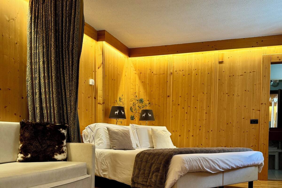 A bedroom with a bed, a sofa, two lamps, a wooden wall, and a cowhide rug.