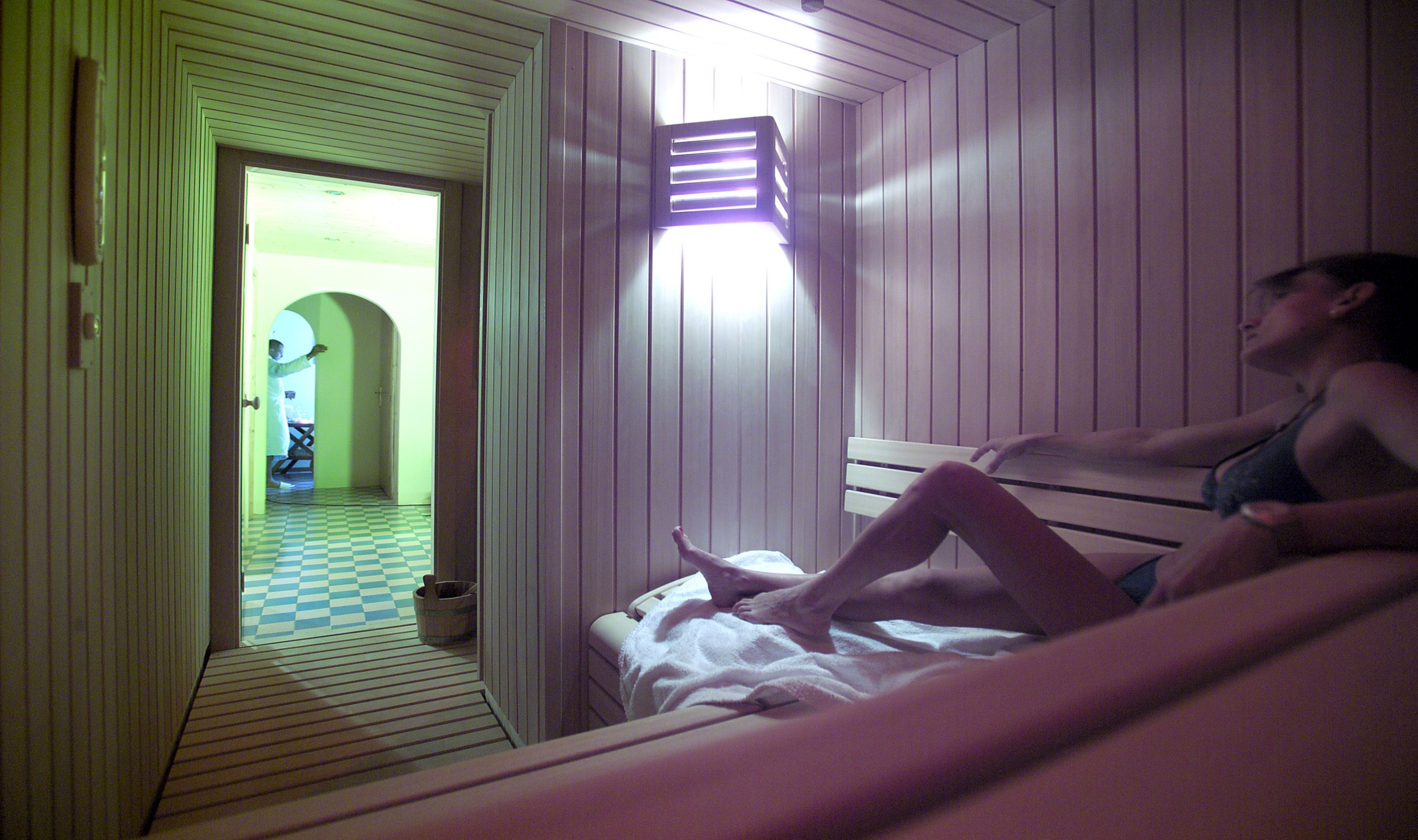 A room with a checkered floor, a bed, a wall-mounted light, and a door leading to another room.