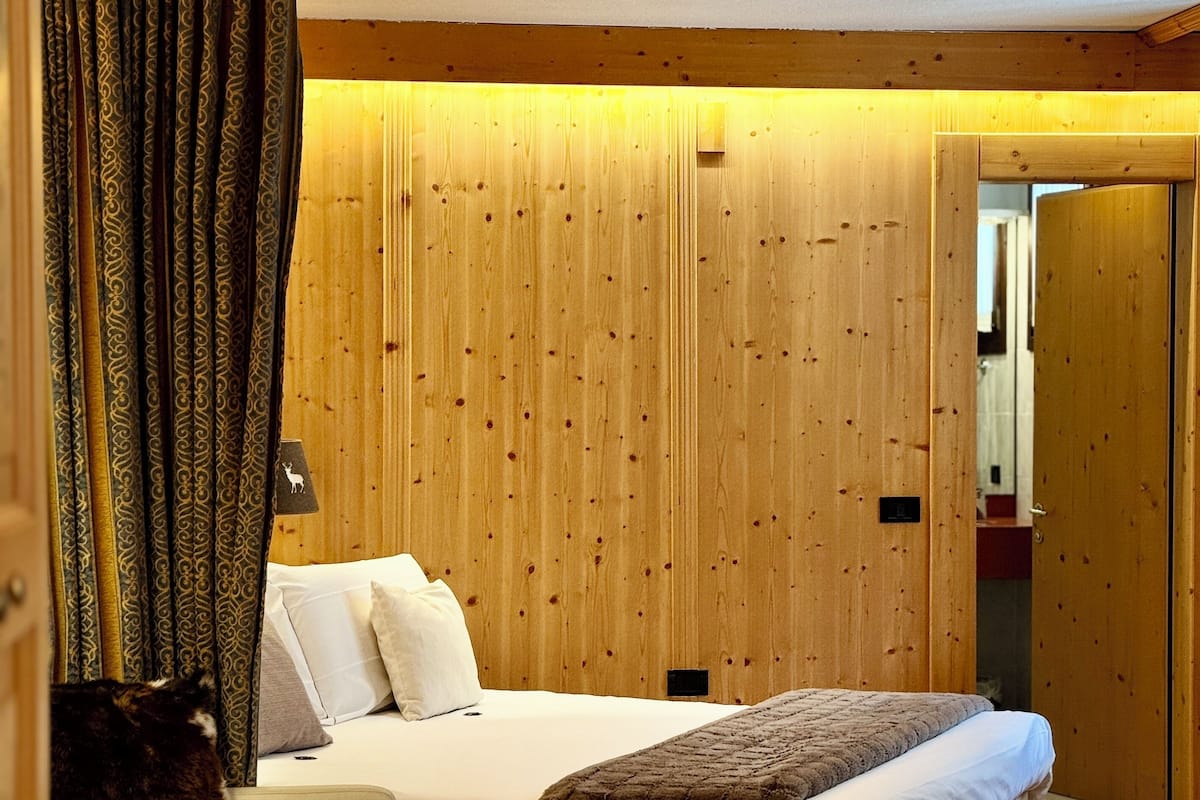 A bedroom with a wooden wall, a bed with white bedding, and a cat on a chair.