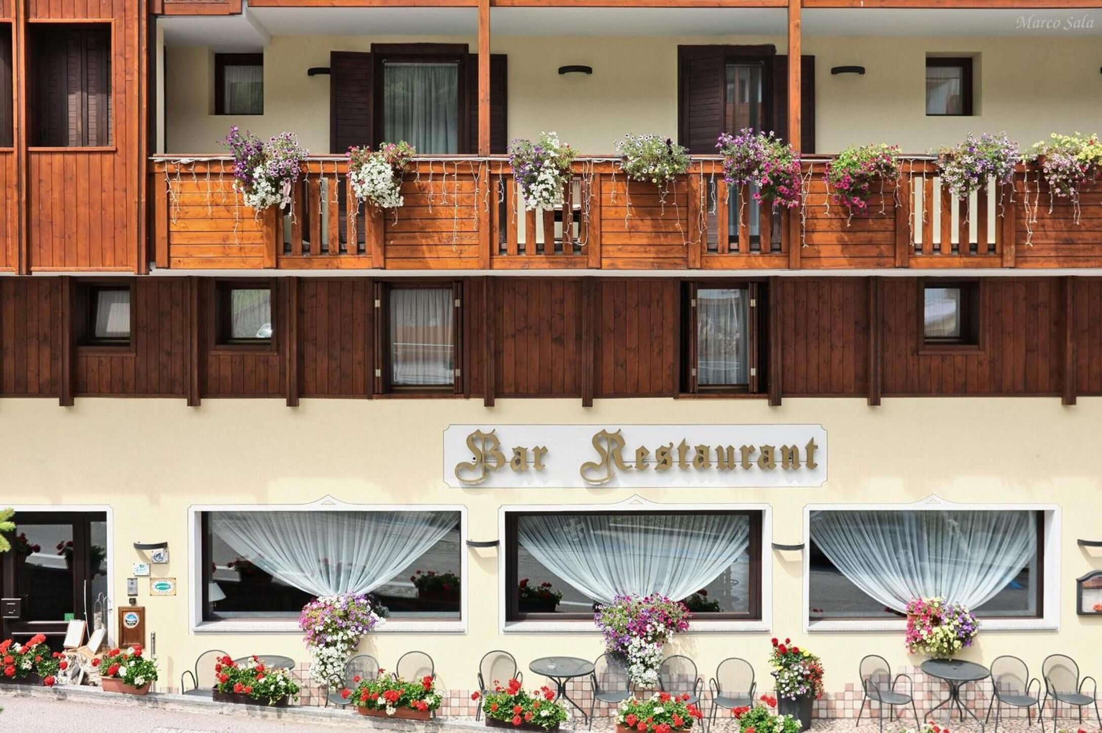 A bar restaurant with a wooden facade, multiple balconies with flower boxes, and outdoor seating with tables and chairs.