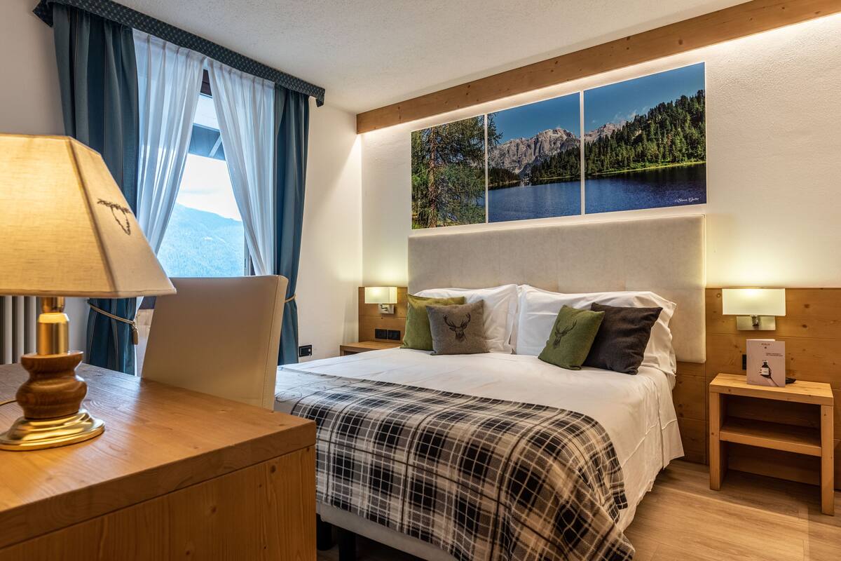 A hotel room with a bed, a desk, a lamp, and a view of mountains through the window.