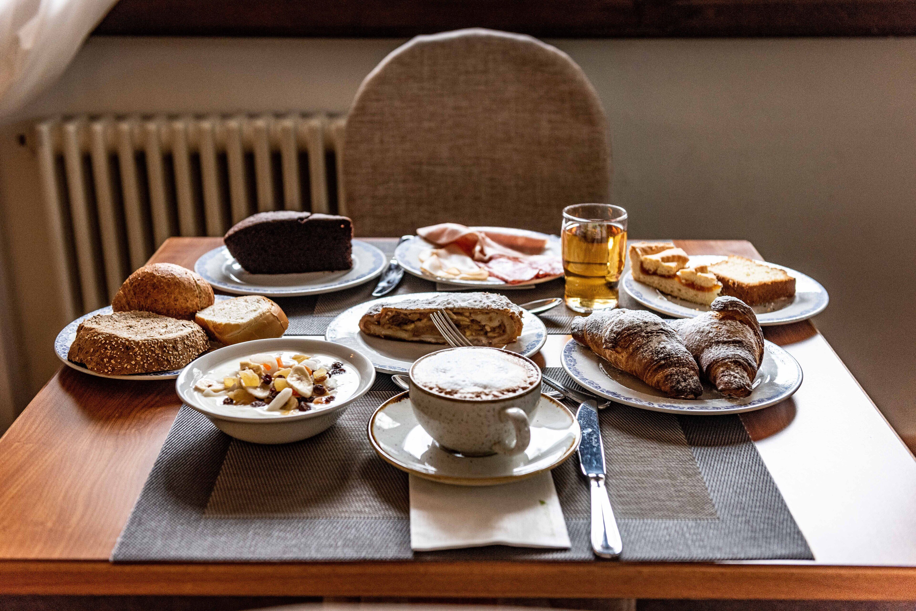 Una mesa servida con diversos productos para el desayuno, como pasteles, pan y una taza de té.