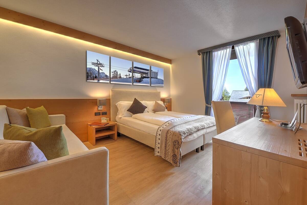 A hotel room with a bed, a desk, a chair, a nightstand, and a window with curtains.