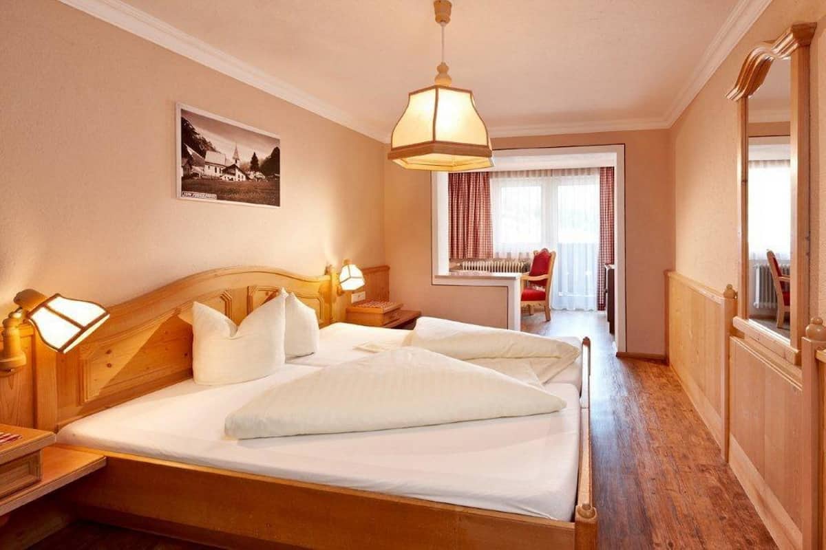 A hotel room with a wooden bed, two bedside lamps, a window with curtains, and a door with a mirror.