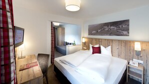 A hotel room with a large bed, a desk with a lamp, a chair, and a painting on the wall. - Hotel Bergland (Sankt Leonhard im Pitztal)