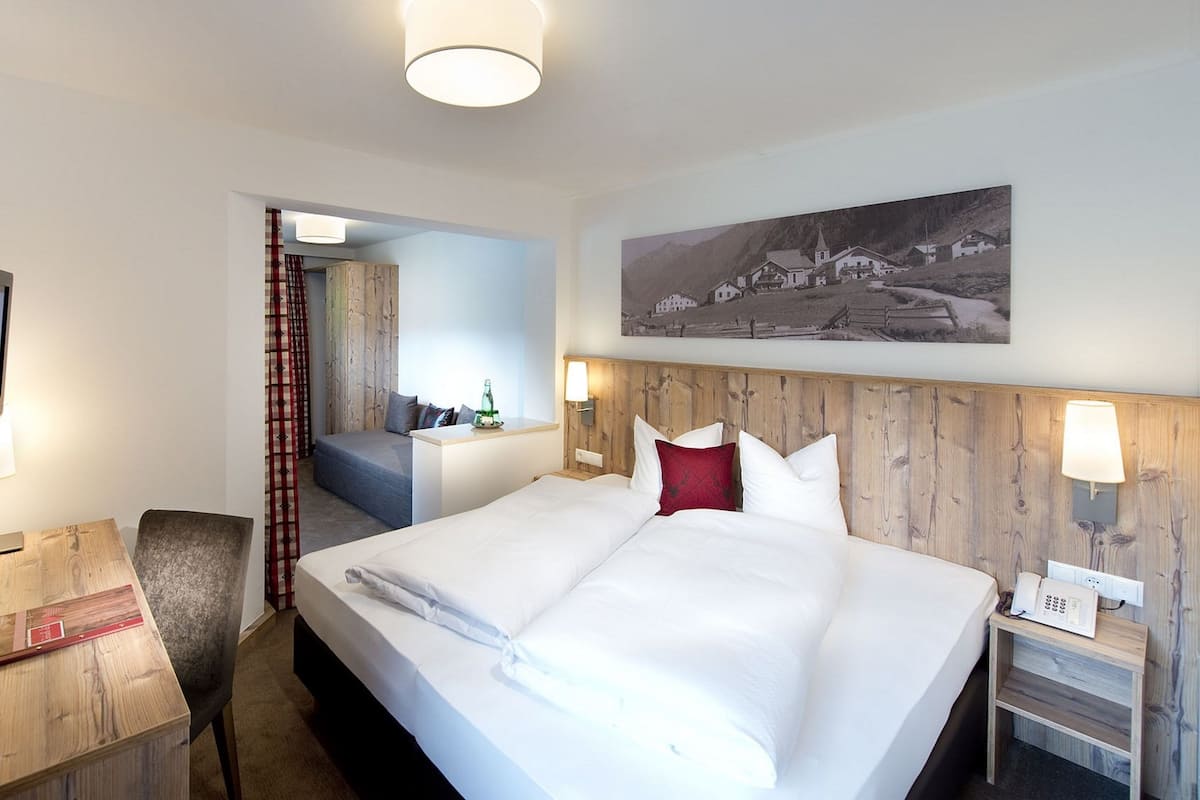 A hotel room with a large bed, a desk with a lamp, a chair, and a painting on the wall.