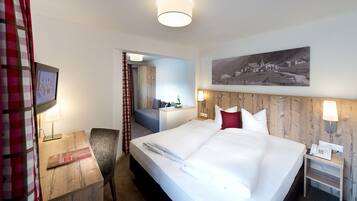 A hotel room with a large bed, a desk with a lamp, a chair, and a painting on the wall.