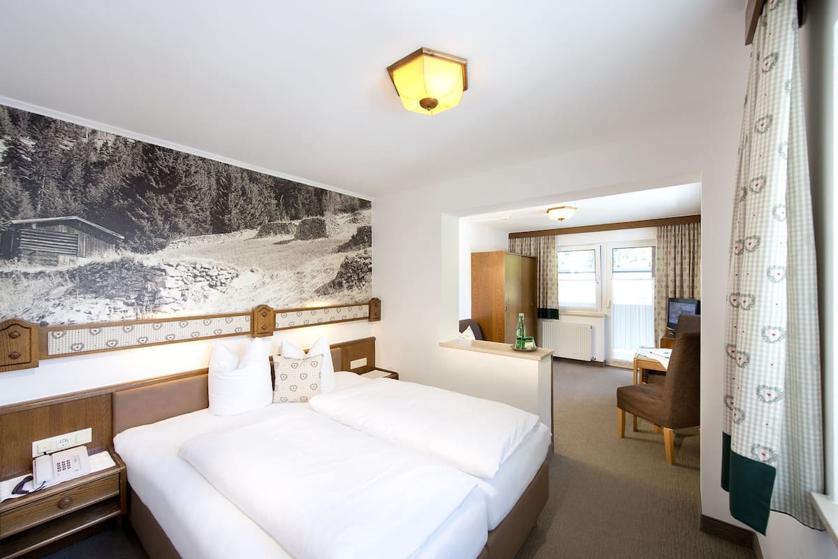 A hotel room with a large bed, a desk with a computer, and a view of a forested area through the window.