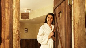 A wooden door with a metal latch, a wooden floor, and a bed with white linens in the background. - Hotel Bergland (Sankt Leonhard im Pitztal)