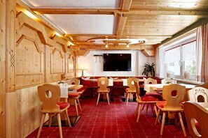 A restaurant with wooden walls and ceiling, red carpet flooring, and wooden chairs with red cushions. - Hotel Bergland (Sankt Leonhard im Pitztal)