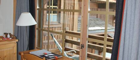 A room with a wooden desk, chair, and a window with a view of a wooden structure outside.