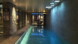 Une piscine intérieure avec un mur en pierre et des portes vitrées donnant accès à une salle de bain.