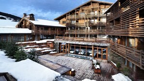 Un chalet en bois doté d’une vaste terrasse et de plusieurs balcons, entouré de neige.