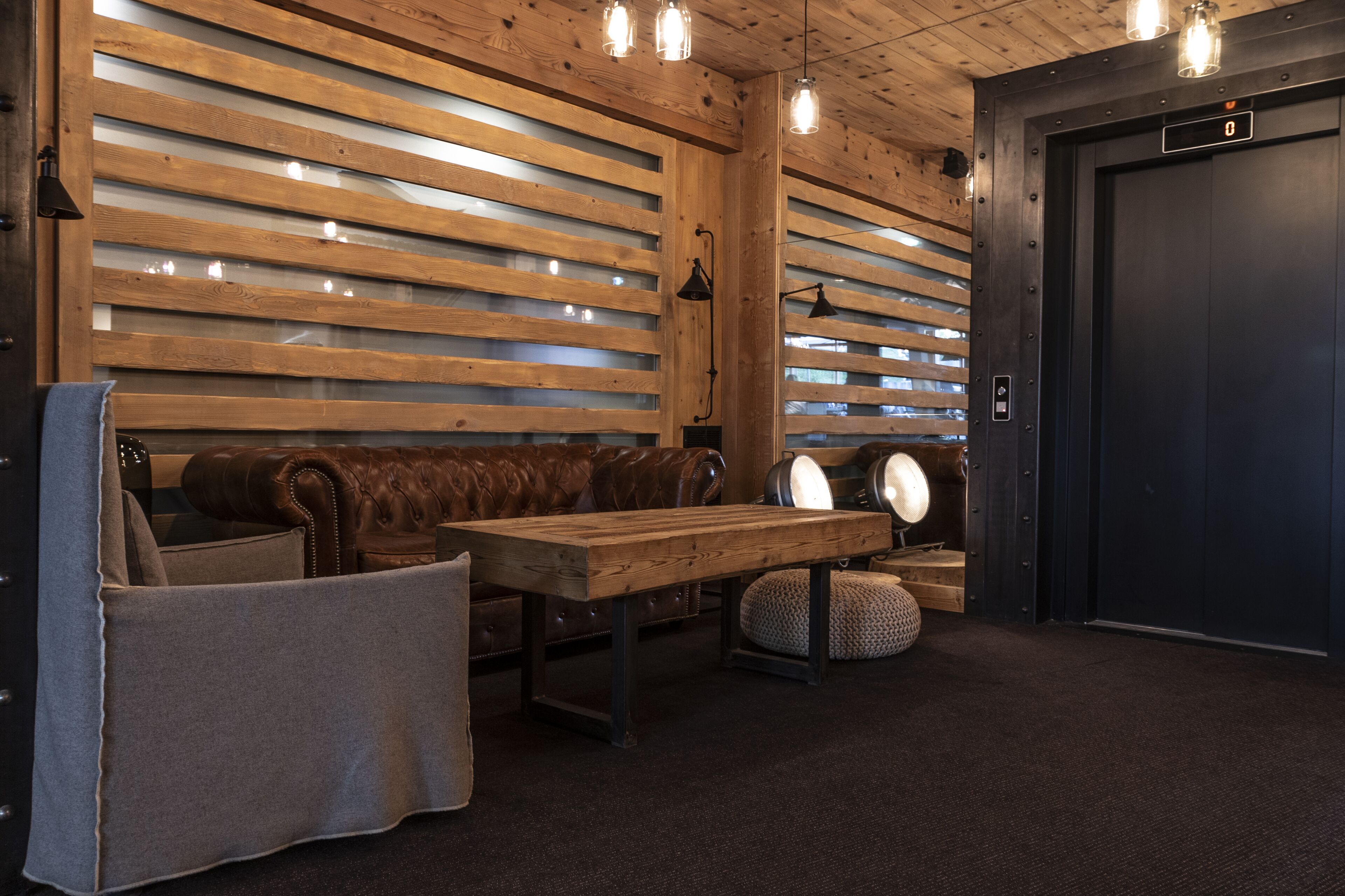 A wooden interior with a leather couch, a wooden table, and a dark elevator door.