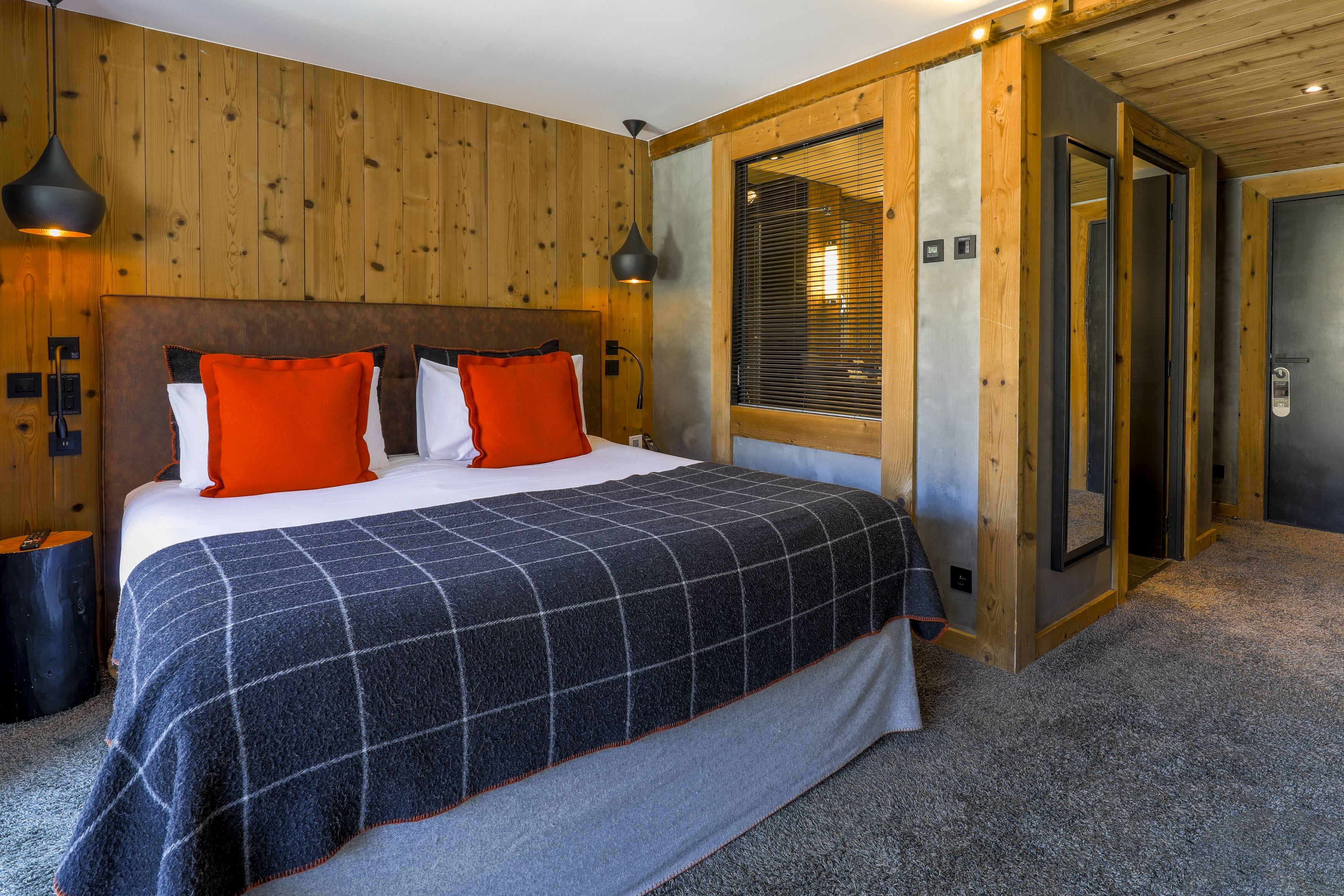 A bedroom with a large bed, wooden walls, a window with blinds, and a door.