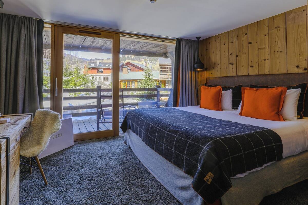 A hotel room with a bed, a chair, a desk, and a view of the outside.