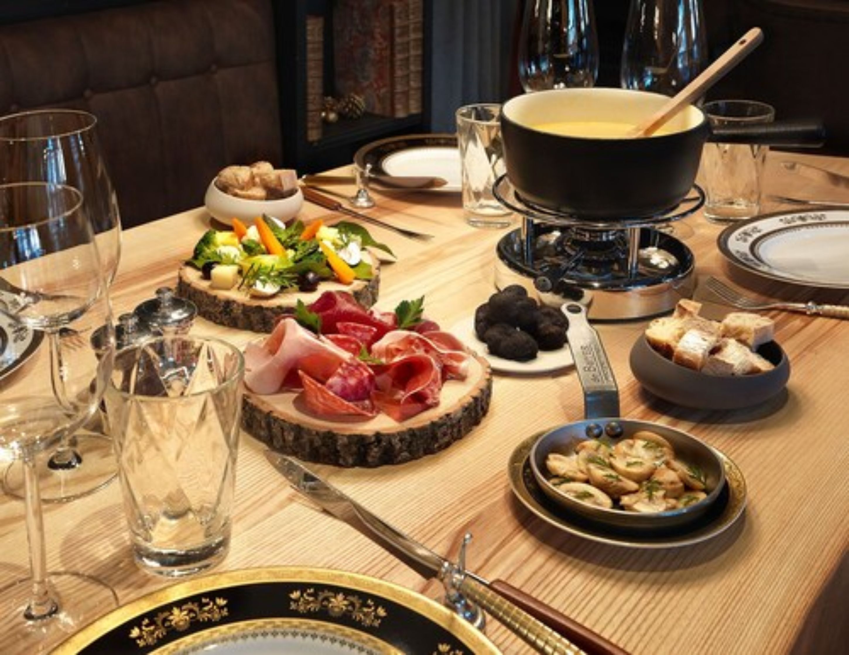 A dining table set with various food items, including a hot pot, charcuterie, and a bowl of mushrooms.