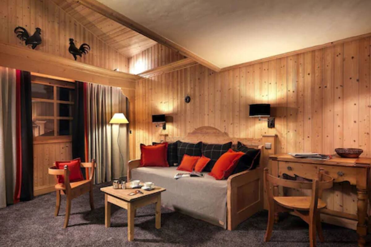 A cozy room with a wooden bed, a small table, a chair, and a desk with a lamp.