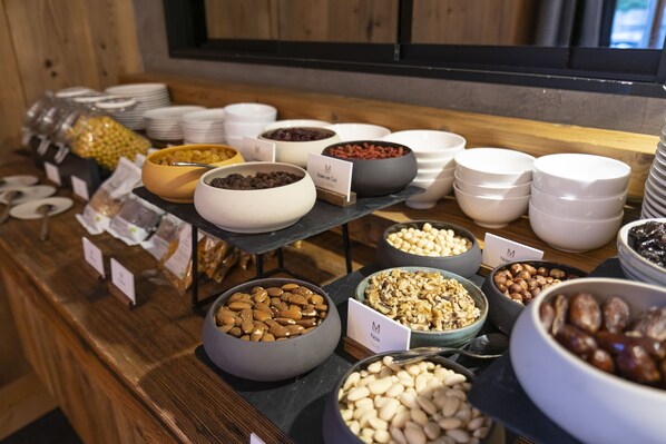A buffet with various bowls of nuts and dried fruits, arranged on a wooden counter with a window in the background. - Le M de Megève (Megeve)