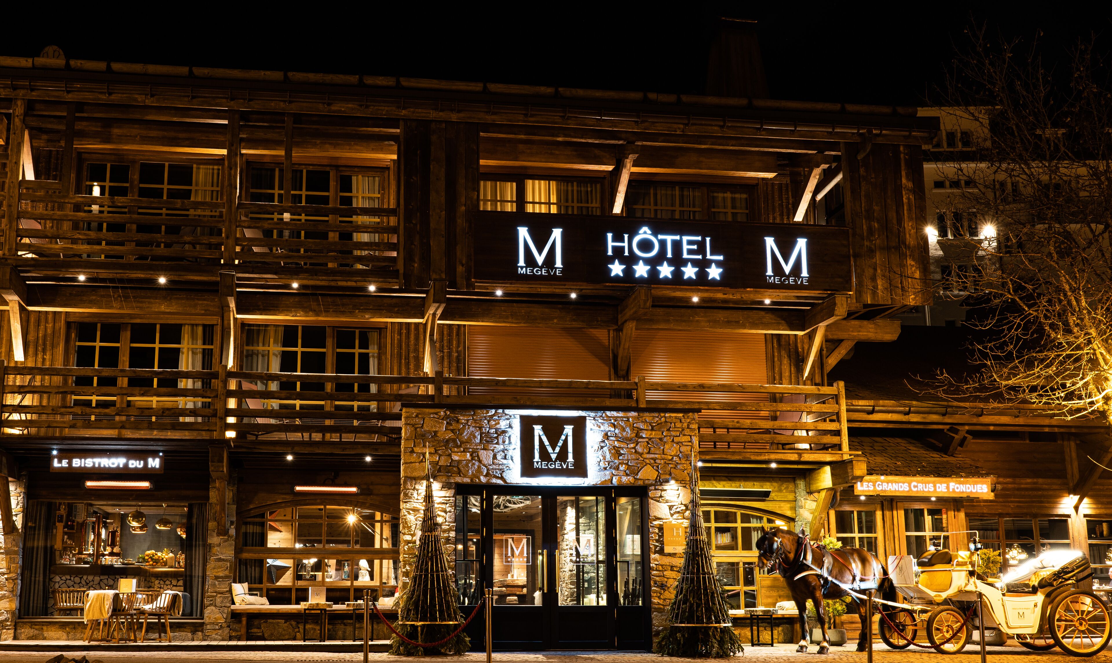 Ein Hotel mit einem auffälligen 'M'-Logo, einer Stein-Fassade und einer Kutsche vor dem Haus.