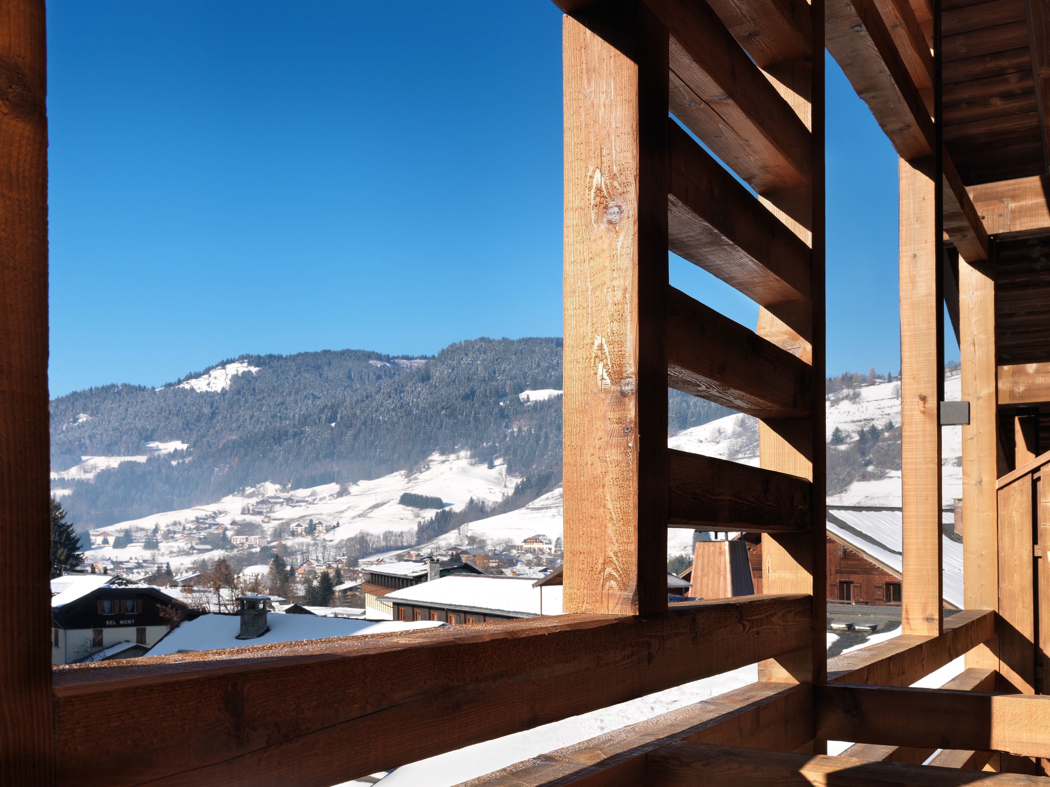 A wooden balcony with a view of a snowy mountain and a village below.