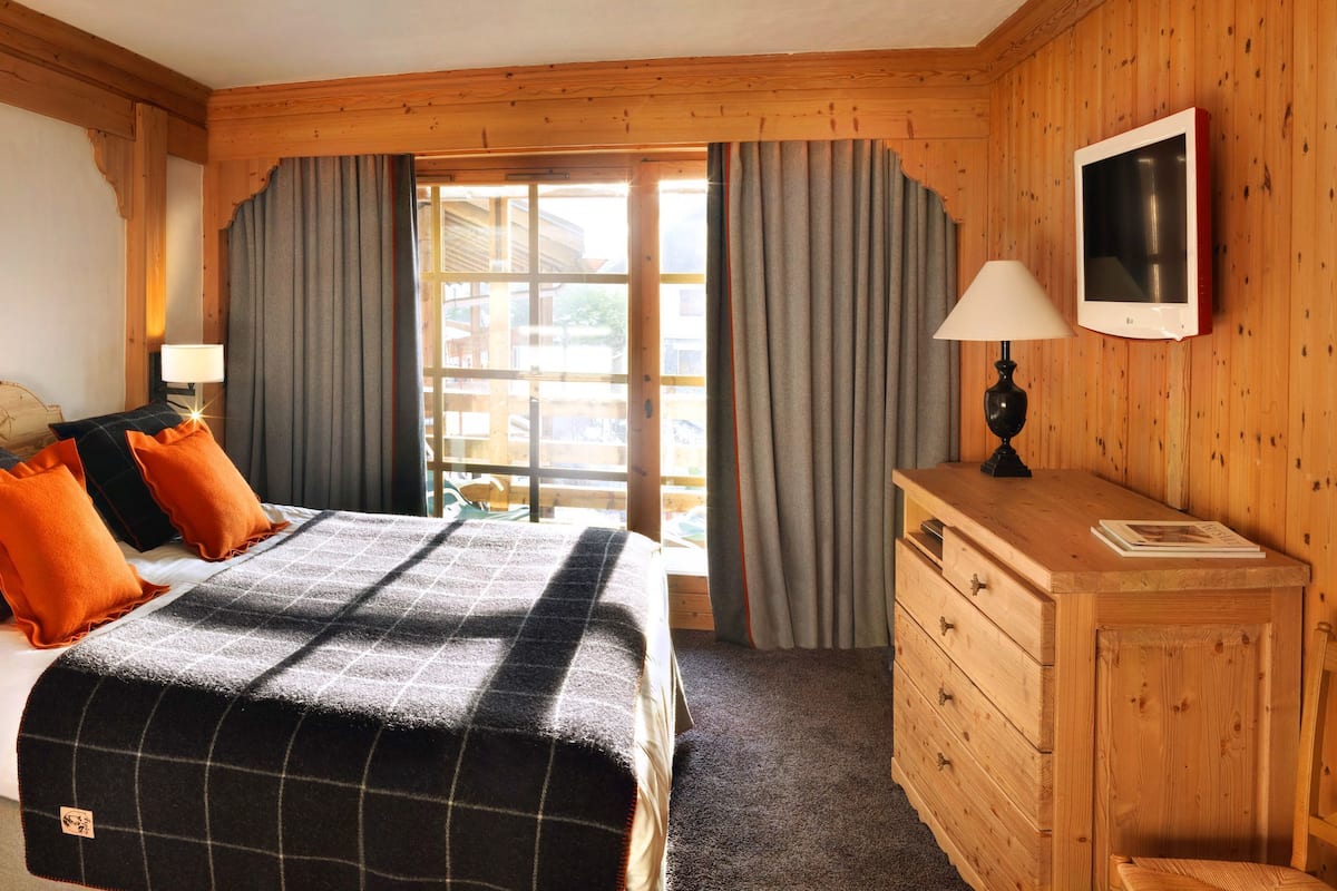 A wooden room with a bed, two bedside lamps, a TV, and a dresser.