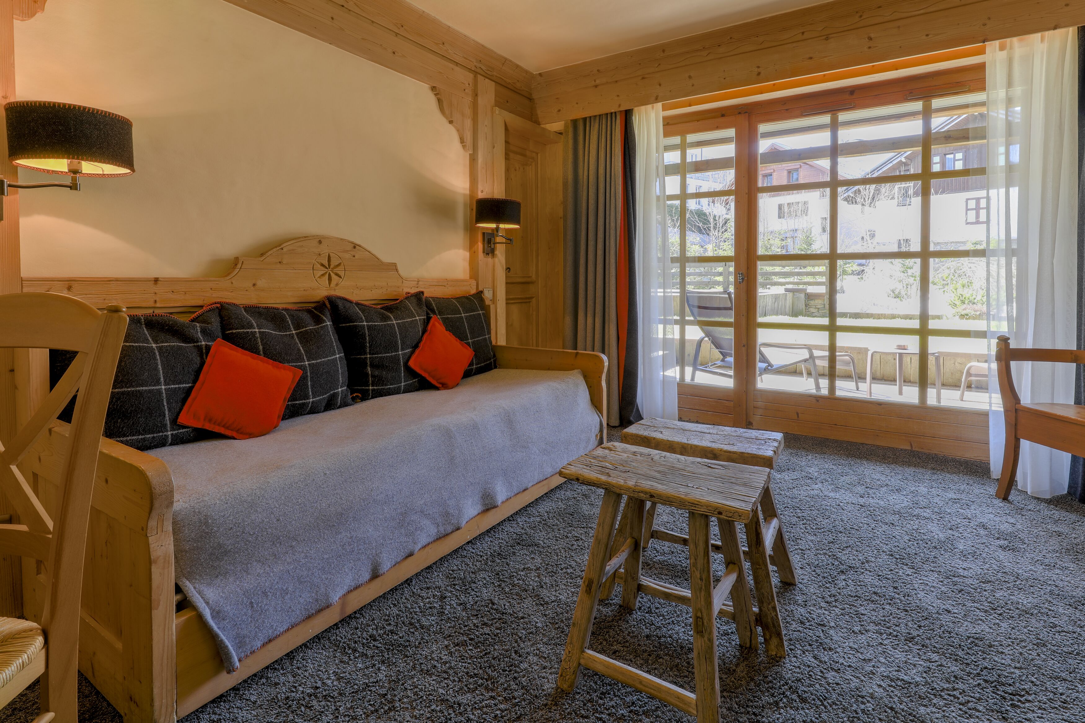 Une pièce chaleureuse avec un canapé en bois, un petit tabouret en bois et une grande fenêtre donnant sur l’extérieur.