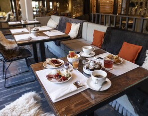 A dining area with tables set for breakfast, including plates of food, cups, and a variety of condiments. - Le M de Megève (Megeve)