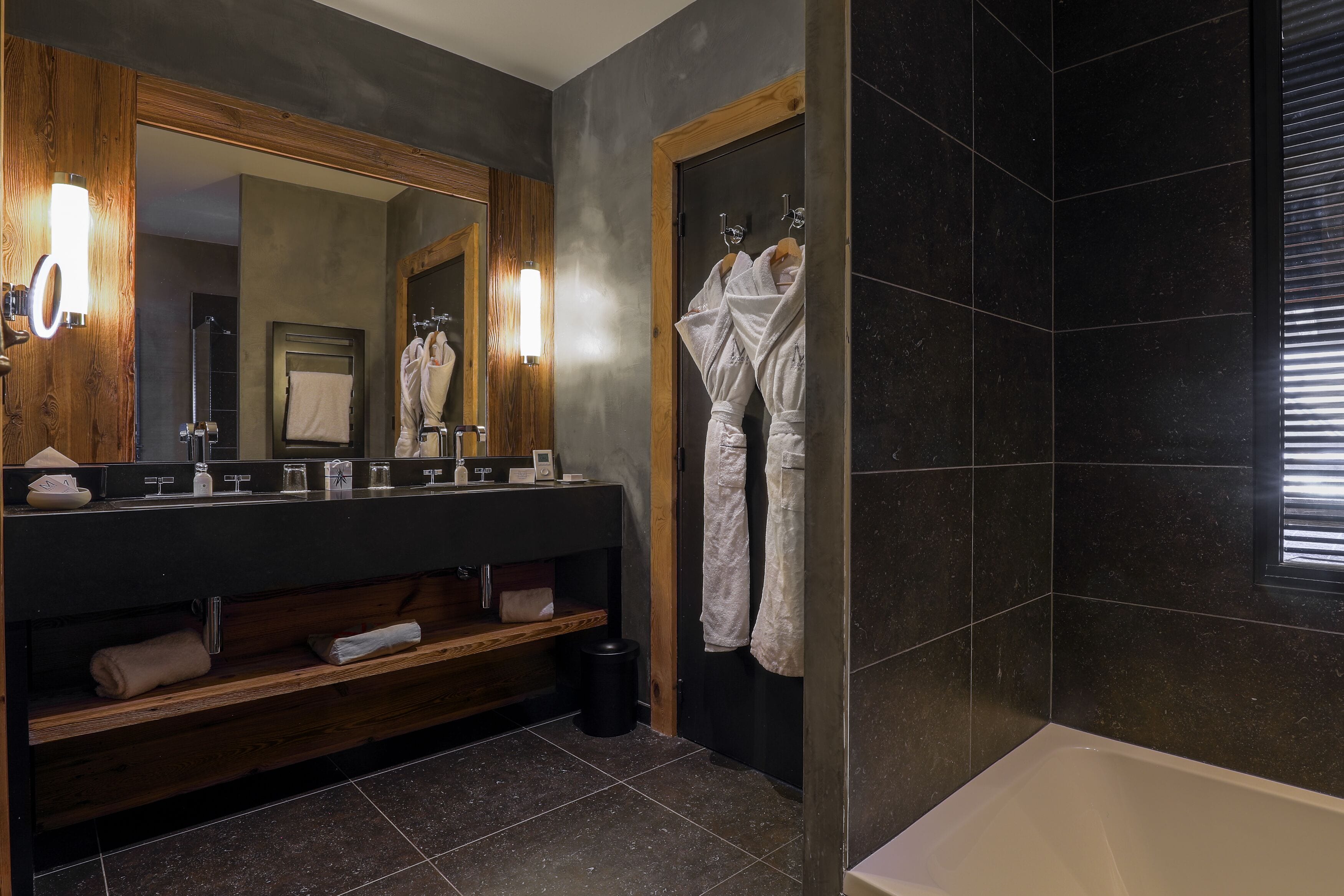 Un baño moderno con ducha de azulejos oscuros, tocador de madera con espejo y bañera.
