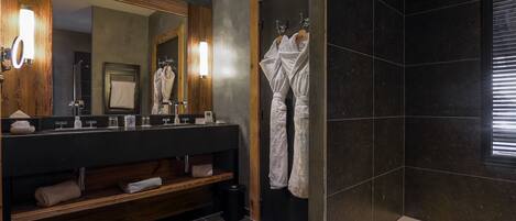 A modern bathroom with a dark tiled shower, a wooden vanity with a mirror, and a bathtub.