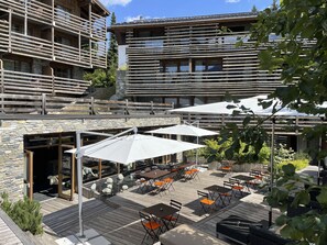 An outdoor patio with tables and umbrellas, stone walls, and a wooden deck. - Le M de Megève (Megeve)
