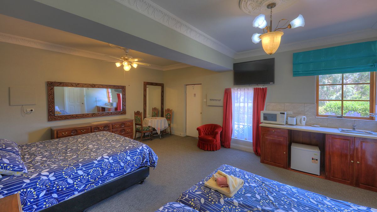 A hotel room with two beds, a desk with a microwave, a TV, and a window with curtains.