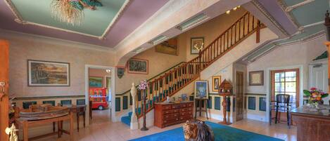 Una habitación amplia con una gran escalera, una mesa de madera y un tapete azul.